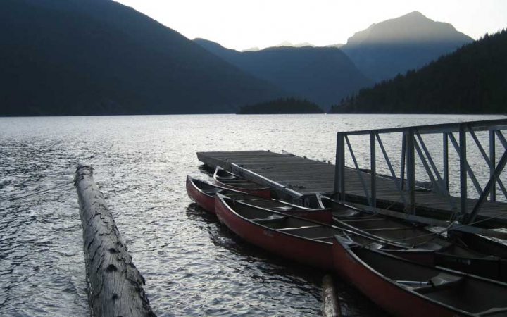 canoes rest beside a dock on a calm lake with mountains in the background